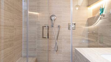 A modern bathroom with a glass-enclosed shower, a large mirror, and a marble-tiled vanity.