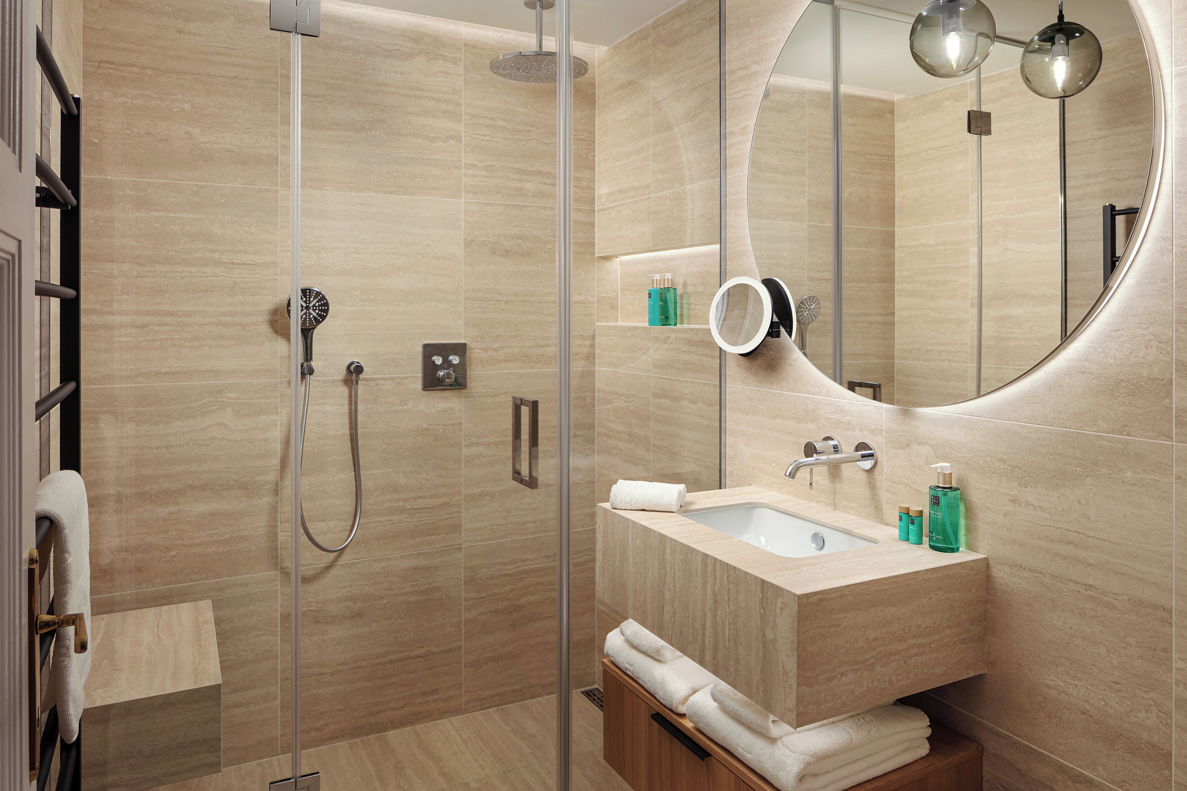 Un baño moderno con ducha de vidrio, un espejo grande y un lavamanos con artículos de aseo.
