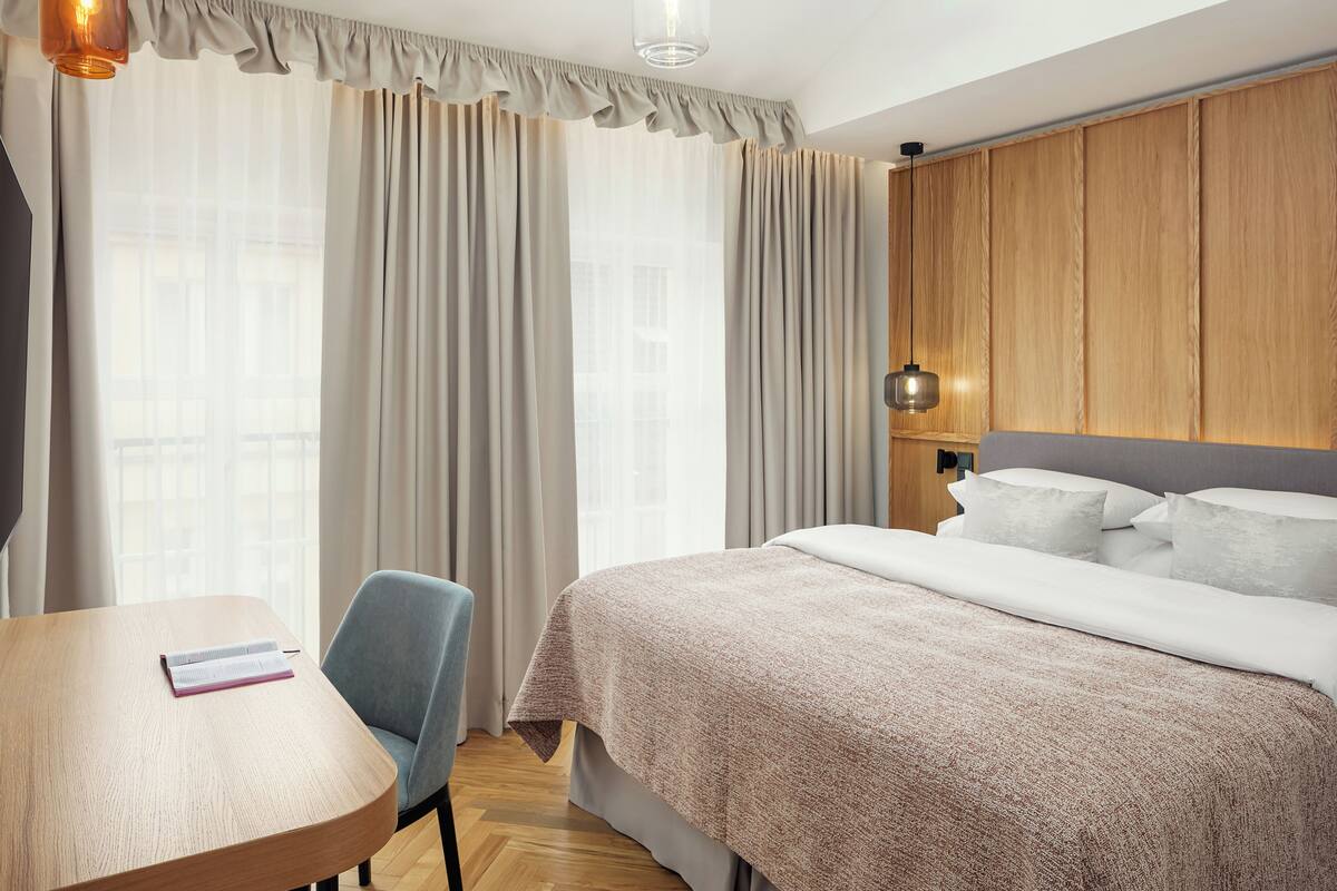 Een hotelkamer met een bed, een bureau, een stoel en een raam met gordijnen.