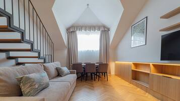 Una sala moderna con piso de espiga, un conjunto de sofá, una mesa de comedor con sillas, un televisor montado en la pared y una escalera con diseño geométrico.