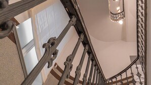 Una escalera con barandillas de metal ornamentadas y un espejo que refleja una habitación con una puerta y una lámpara.
