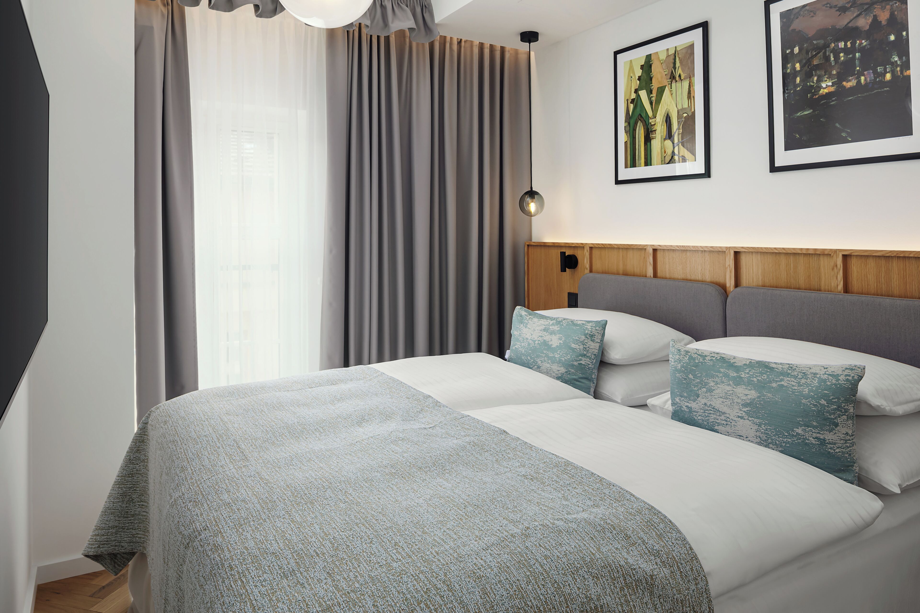 A neatly made bed with a grey and white duvet, a wooden headboard, and two pillows with a distressed blue design.