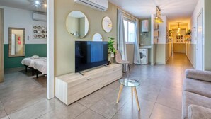 Una sala de estar moderna con un televisor de pantalla plana sobre un mueble de madera, una mesa de centro de vidrio y una zona de estar con sofá y sillones.