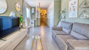 Una sala de estar moderna con un televisor de pantalla plana, un sofá, una mesa de centro de vidrio y un comedor con mesa y sillas.