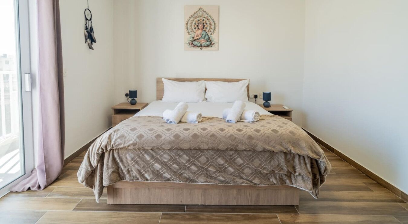 A neatly made bed with a patterned bedspread, two bedside tables with lamps, and a wall hanging above the bed.