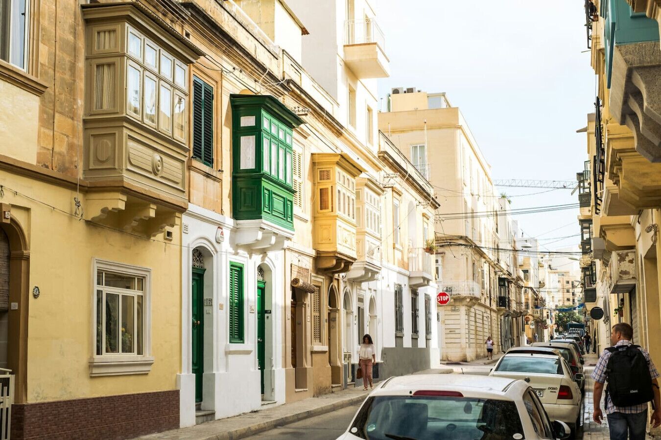 Una calle estrecha flanqueada por edificios históricos, con varios coches aparcados y un peatón caminando.