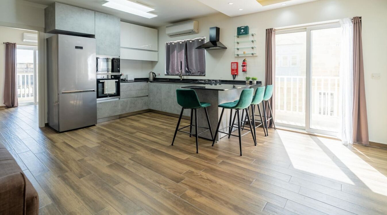 A modern kitchen with a central island, bar stools, and a view to the outside.