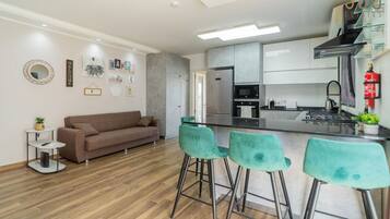 A modern kitchen with stainless steel appliances, a bar area with green bar stools, and a brown sofa in a living area.