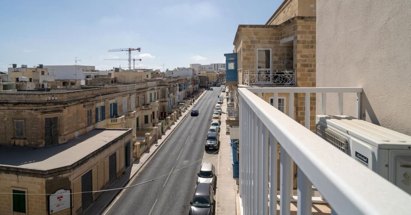 A street view with buildings, a clear sky, and parked cars.