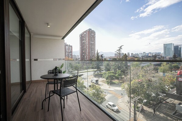 A balcony with a table and chairs, offering a view of a cityscape with buildings and a road. - Asturias Apartments by Andes STR (Santiago)