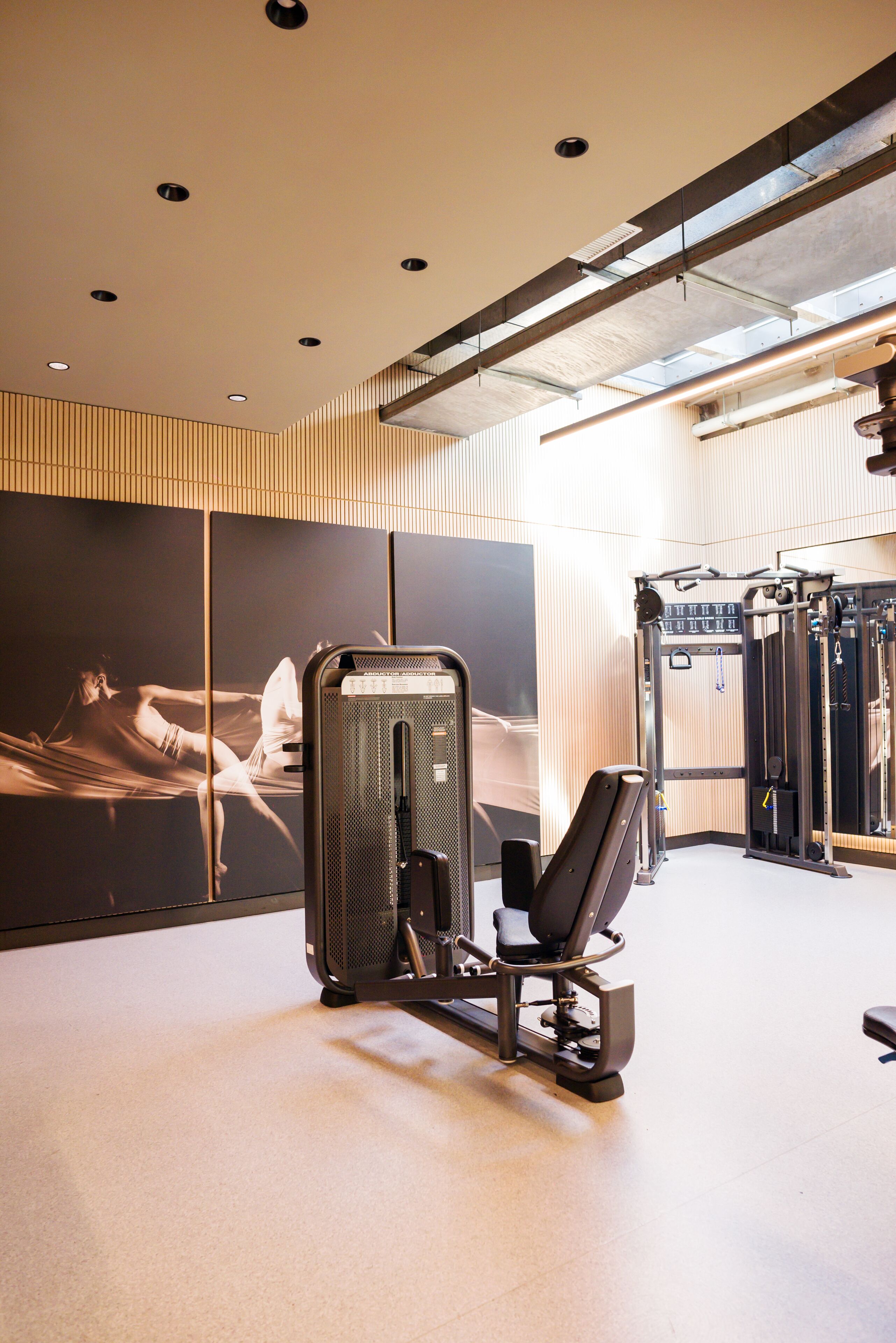 Un gimnasio con equipo de ejercicio, una pantalla montada en la pared e iluminación empotrada en el techo.