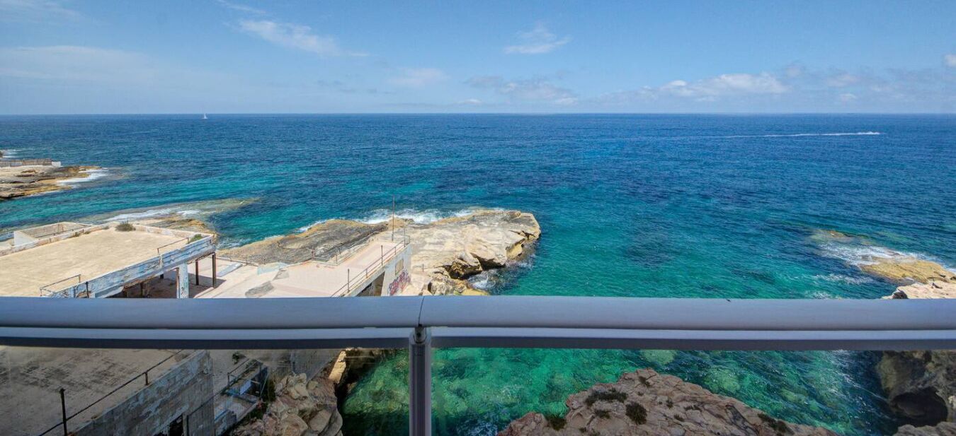 A coastal view with clear blue waters, rocky terrain, and a bridge.