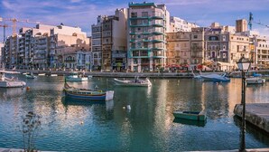 Un paisaje urbano frente al agua, con edificios, barcos y un río tranquilo.