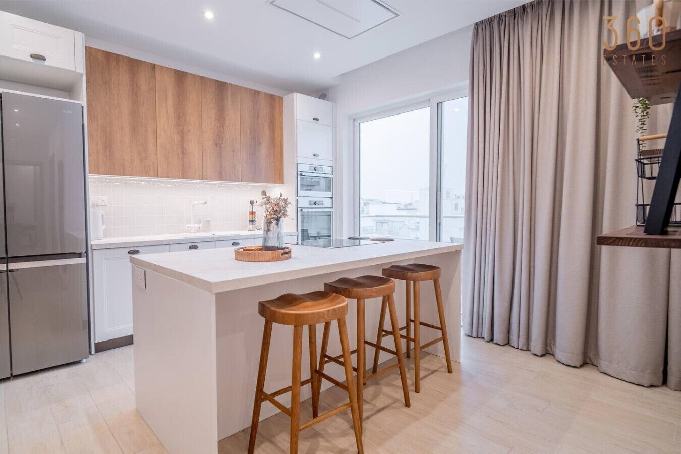 Una cocina moderna con armarios de madera, una isla grande con taburetes y vistas a la ciudad a través de ventanas amplias.