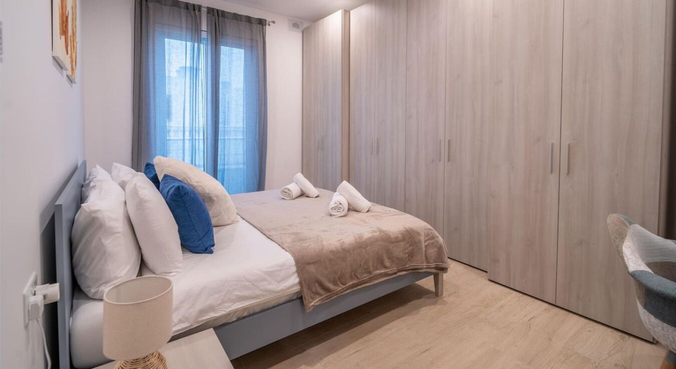 Un dormitorio con cama, una silla, un armario y una ventana con cortinas.