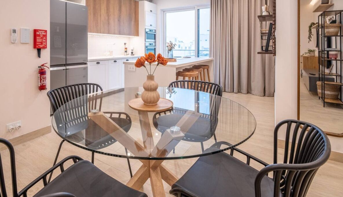 Una cocina moderna con refrigerador, horno y un comedor con mesa y sillas de vidrio.
