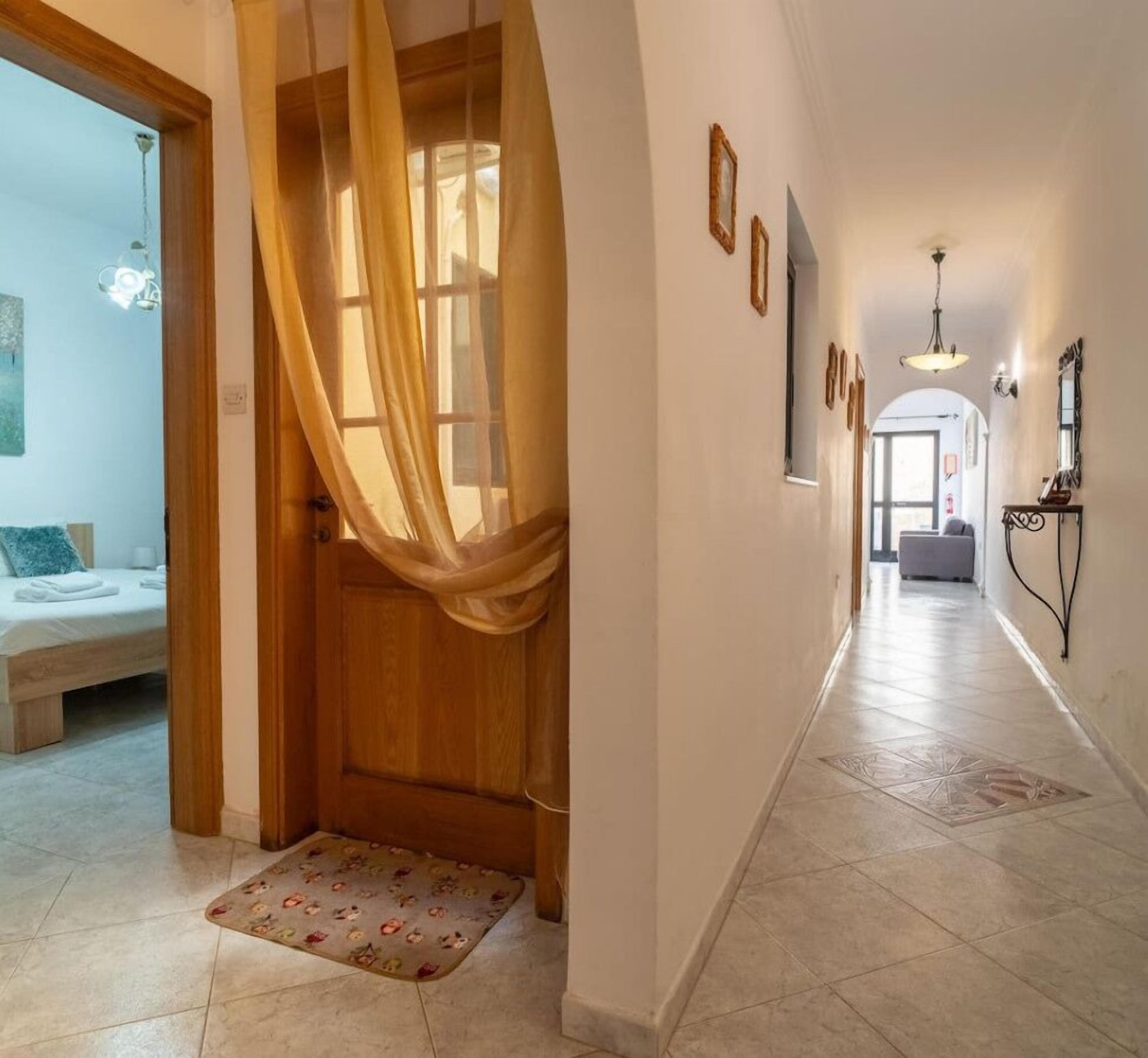 Um corredor com porta de madeira, cama com travesseiro azul e tapete pequeno.