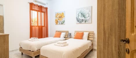 A bedroom with two wooden beds, orange curtains, and floral artwork on the walls.