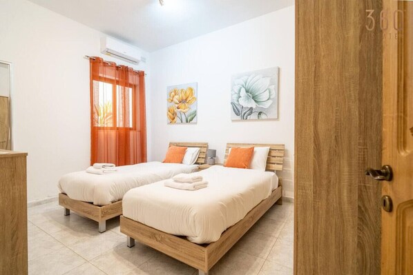 A bedroom with two wooden beds, orange curtains, and floral artwork on the walls.