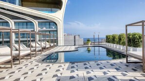 A rooftop pool area with lounge chairs, a swimming pool, and a view of the sea.