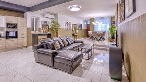 A modern living room with a leather sofa, dining area, kitchen, and a large Buddha statue. - Lovely 3BR maisonette, spacious w/Wifi, AC & Pool (Swieqi)