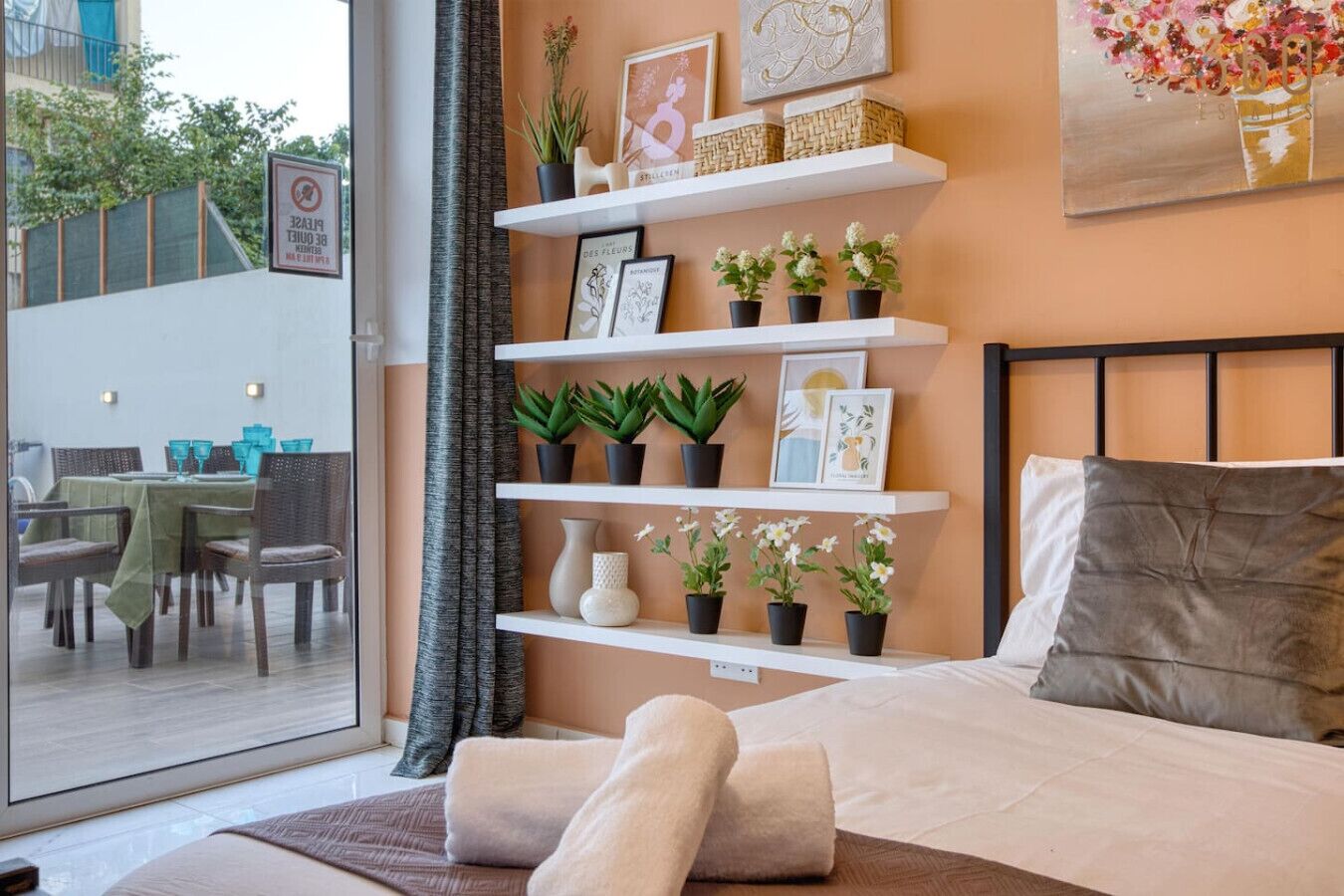 A bedroom with a bed, a window, and a view of an outdoor dining area.