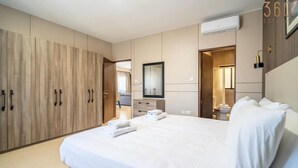 Ein modernes Hotelzimmer mit einem großen Bett, einem Kleiderschrank, einem Badezimmer und einem Spiegel.