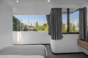 Habitación de hotel moderna con un ventanal grande, una cama y vistas a la ciudad.