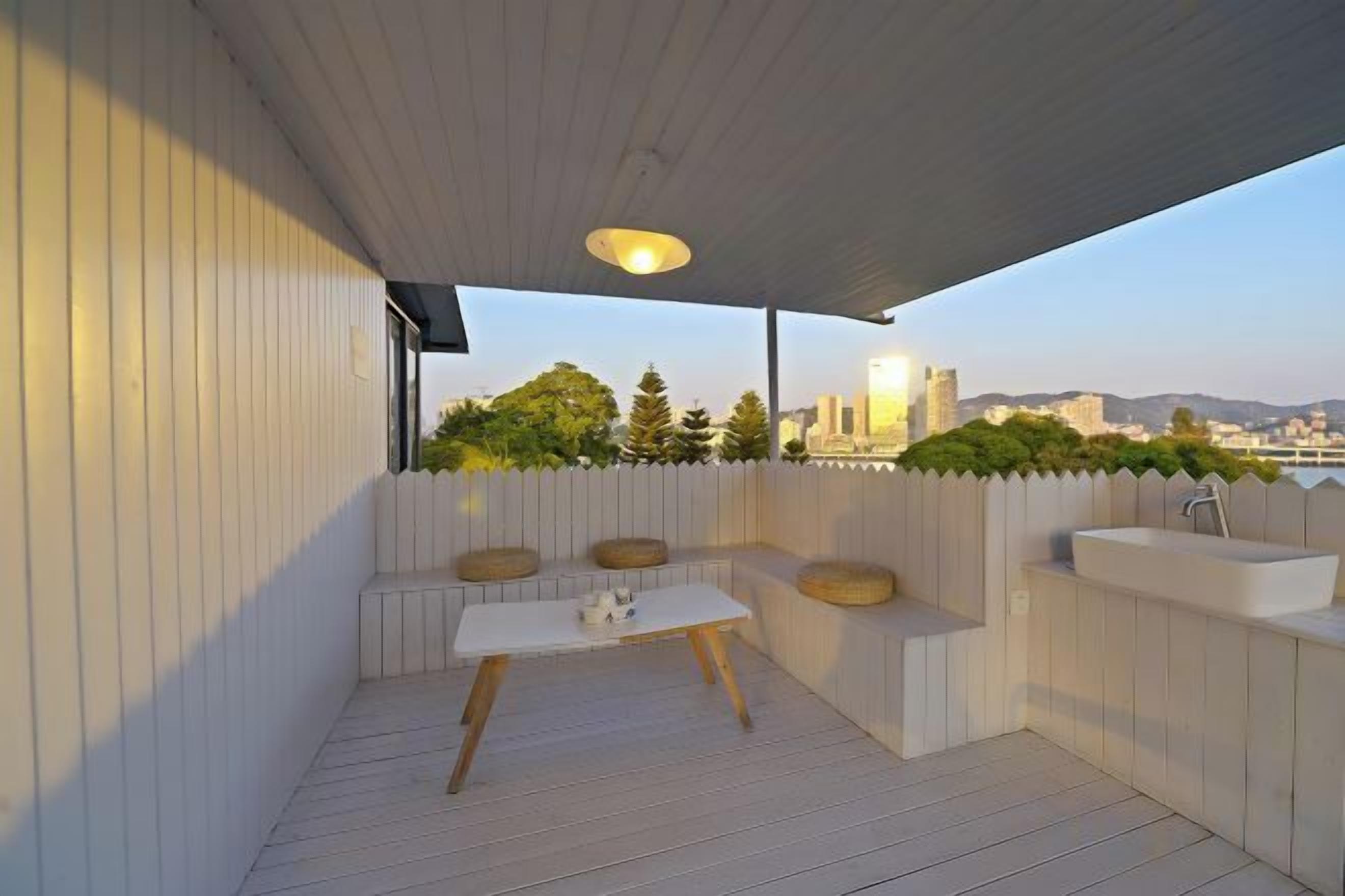 A covered outdoor seating area with a table and benches, overlooking a cityscape.