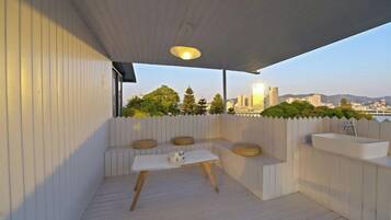 A covered outdoor seating area with a table and benches, overlooking a cityscape.