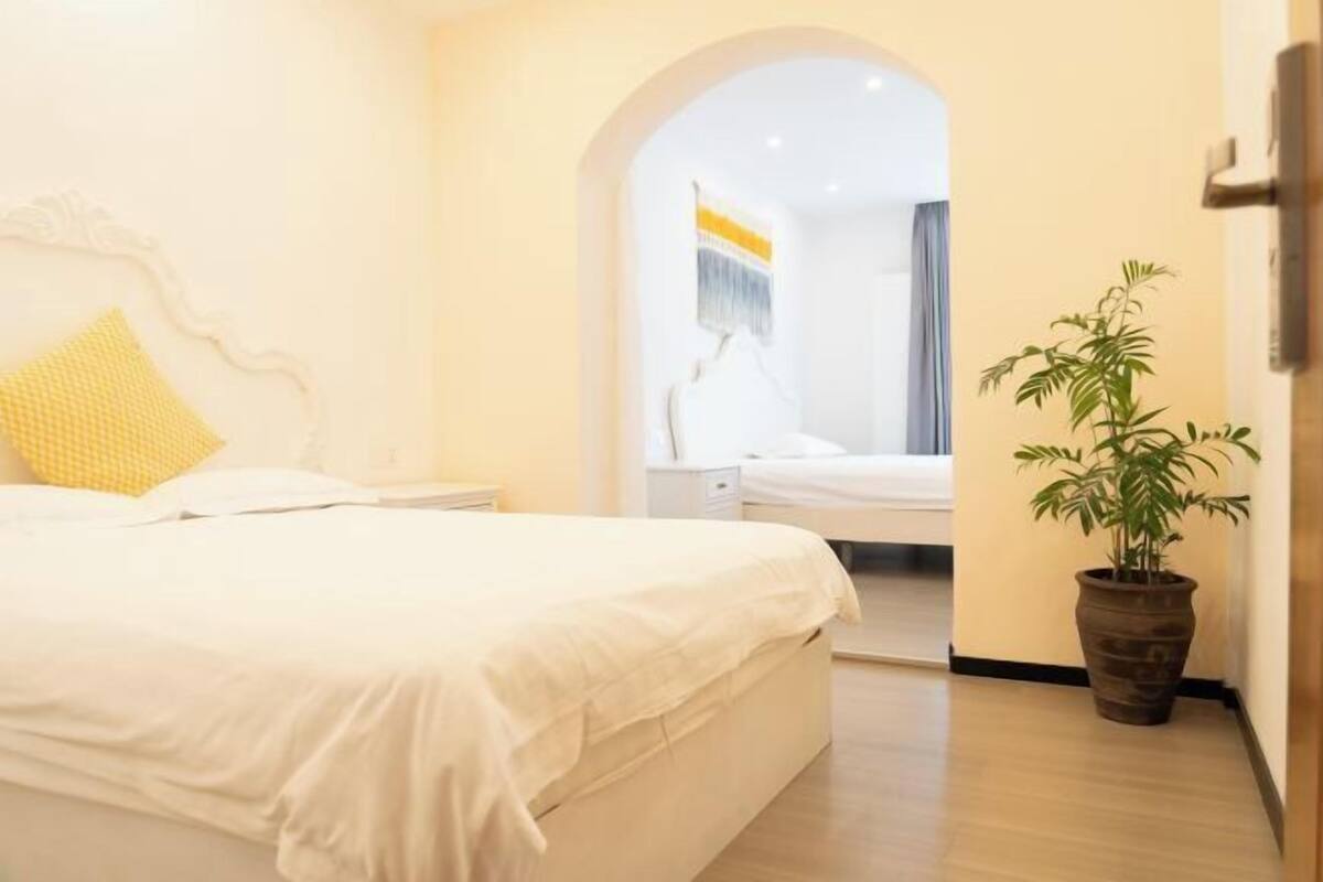 A hotel room with a bed, a nightstand, a potted plant, and an arched doorway leading to another room.
