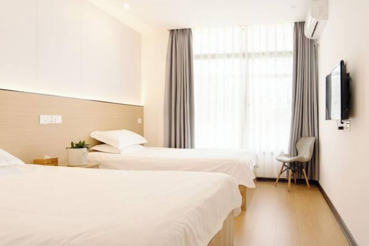 A hotel room with two beds, a TV, a chair, and a window with curtains.