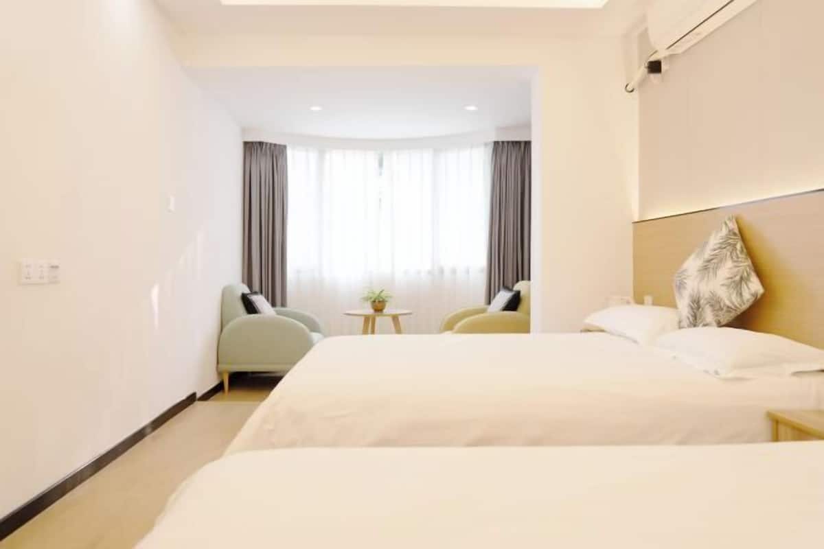 A hotel room with a bed, two chairs, a small table with a plant, and a view of the outside through a window with curtains.