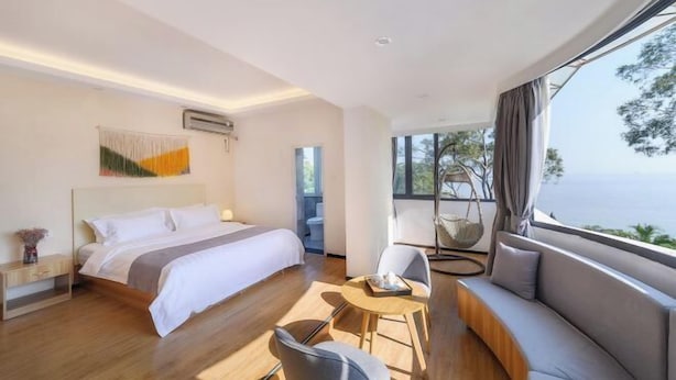 Una habitación de hotel moderna con una cama grande, un sofá, una mesita y vistas al mar.