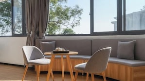 Una sala de estar moderna con un sofá, dos sillones, una mesa redonda de madera y vistas a árboles a través de amplios ventanales.