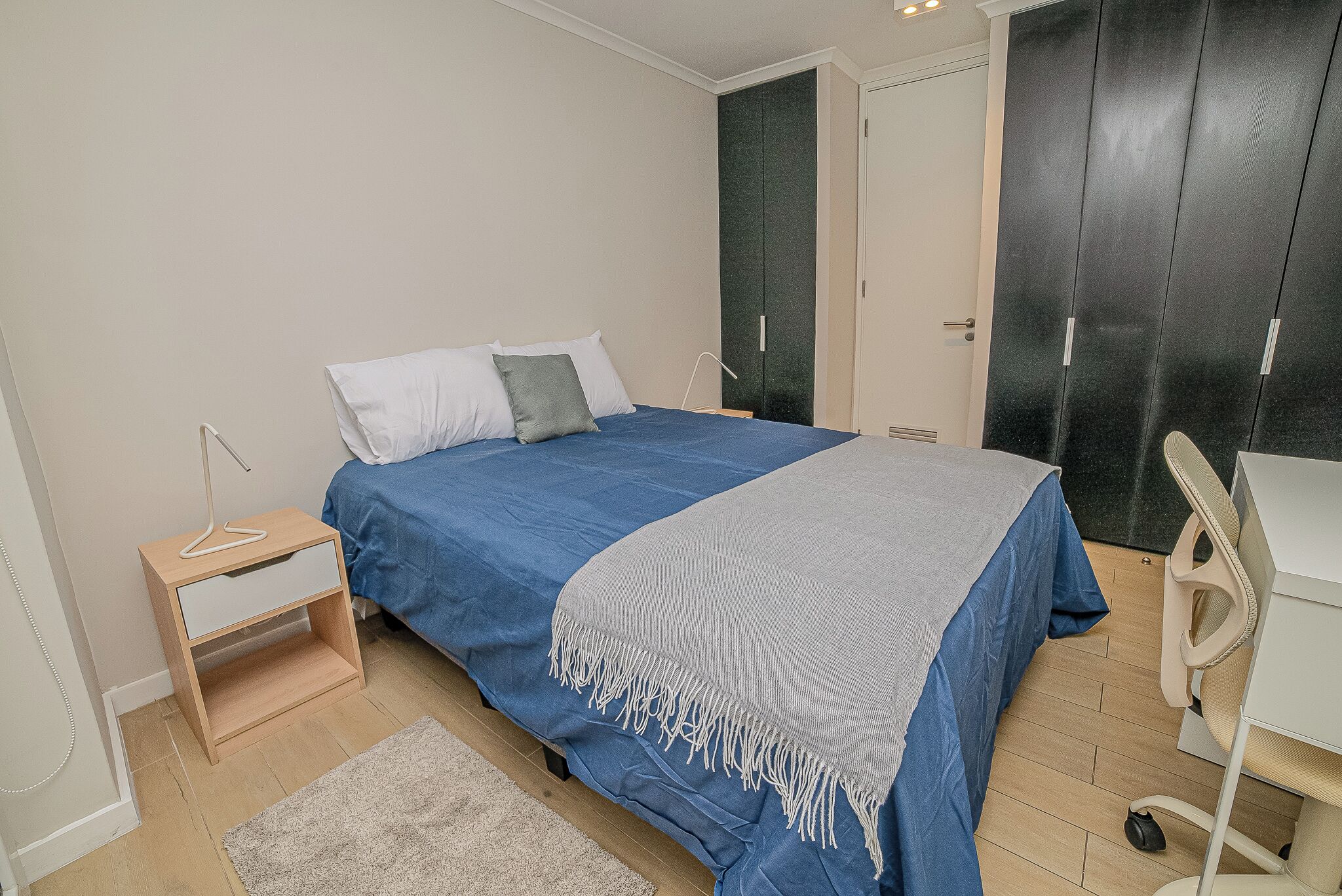 A bedroom with a bed, bedside table, and a desk with a chair.