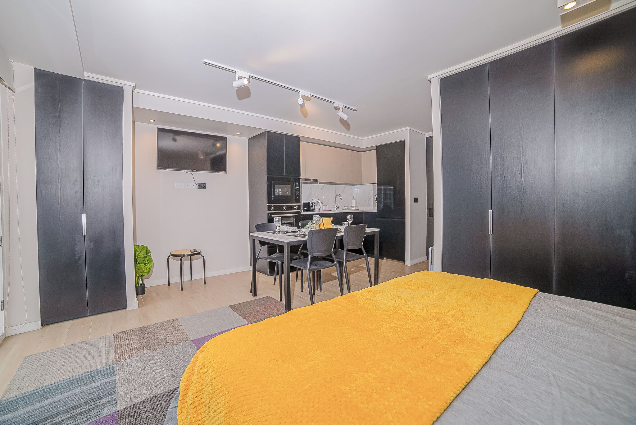 Een moderne slaapkamer met een groot bed, een bureau en een kitchenette op de achtergrond.