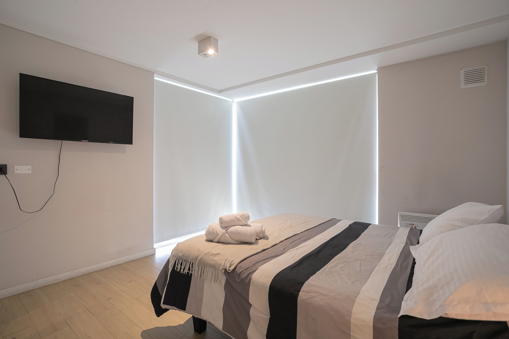 A modern hotel room with a large bed, a flat-screen TV mounted on the wall, and a bedside table.