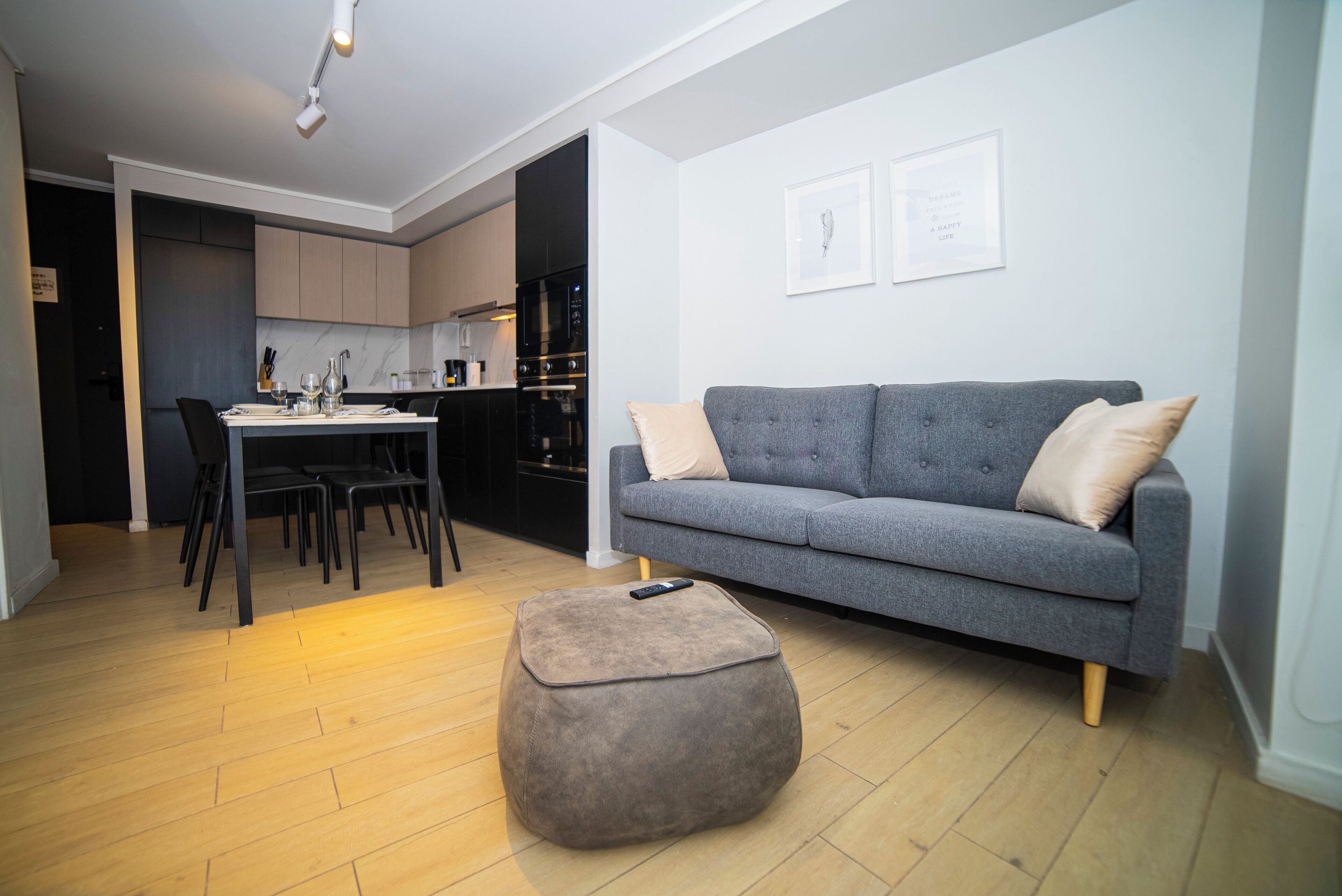 Una sala moderna con un sofá gris, un reposapiés y una zona de comedor con sillas y una mesa.