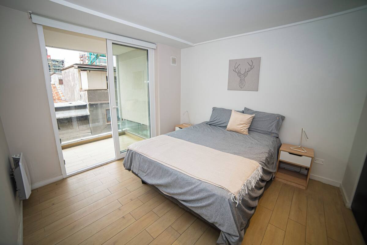 Une chambre à coucher comprenant un lit, une table de chevet, une porte-fenêtre coulissante donnant sur un balcon et une œuvre d’art accrochée au mur.