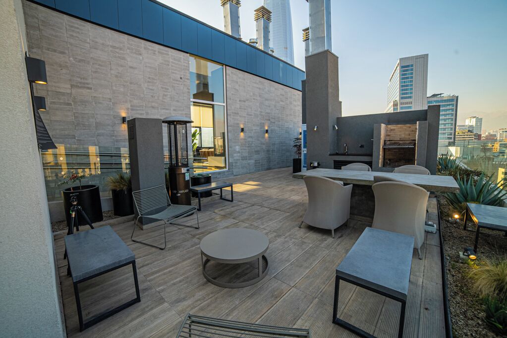An outdoor patio with modern furniture, a grill, and a view of the city skyline.
