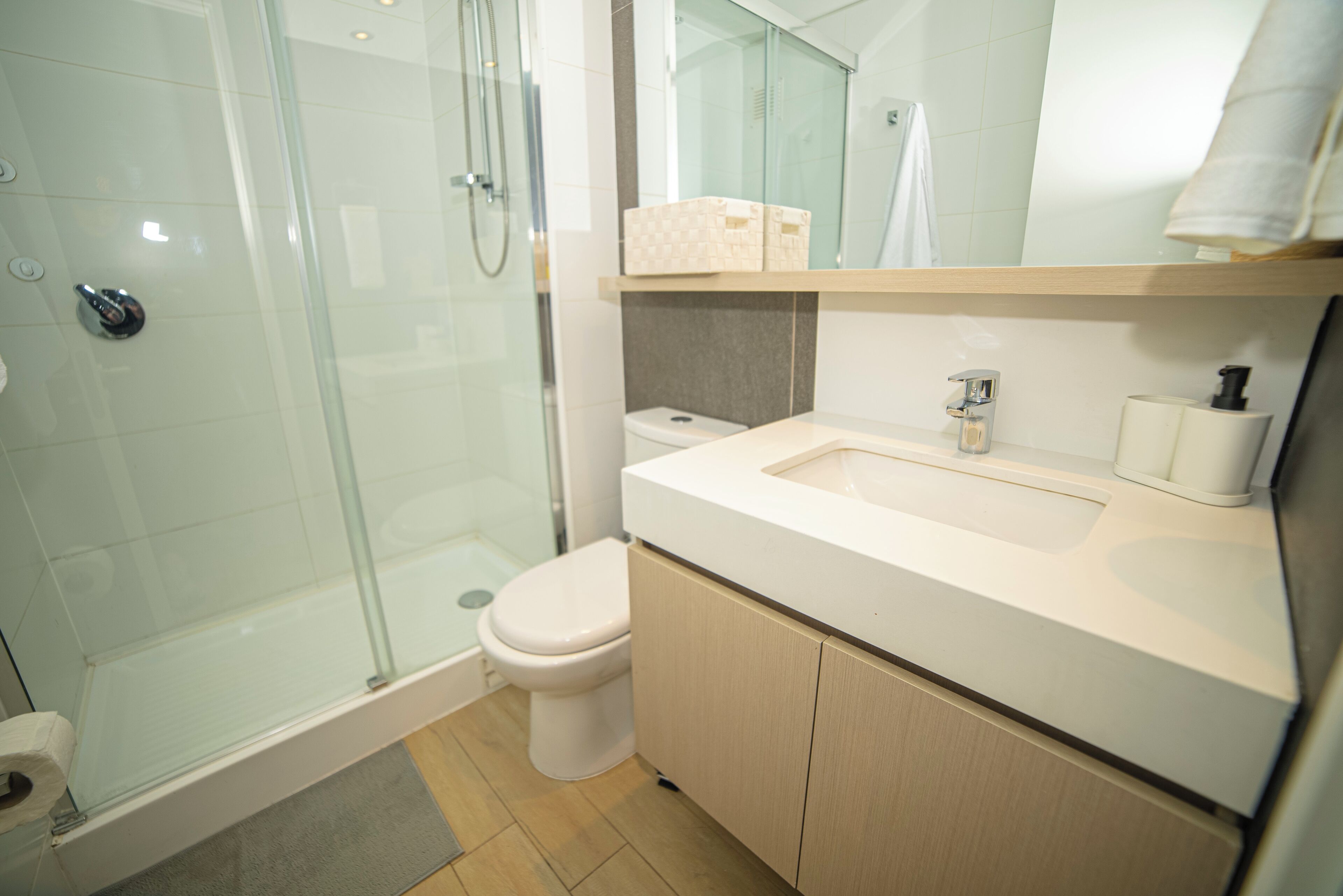 Et moderne badeværelse med en glasafskærmet brusekabine, toilet og et spejl over vasken.
