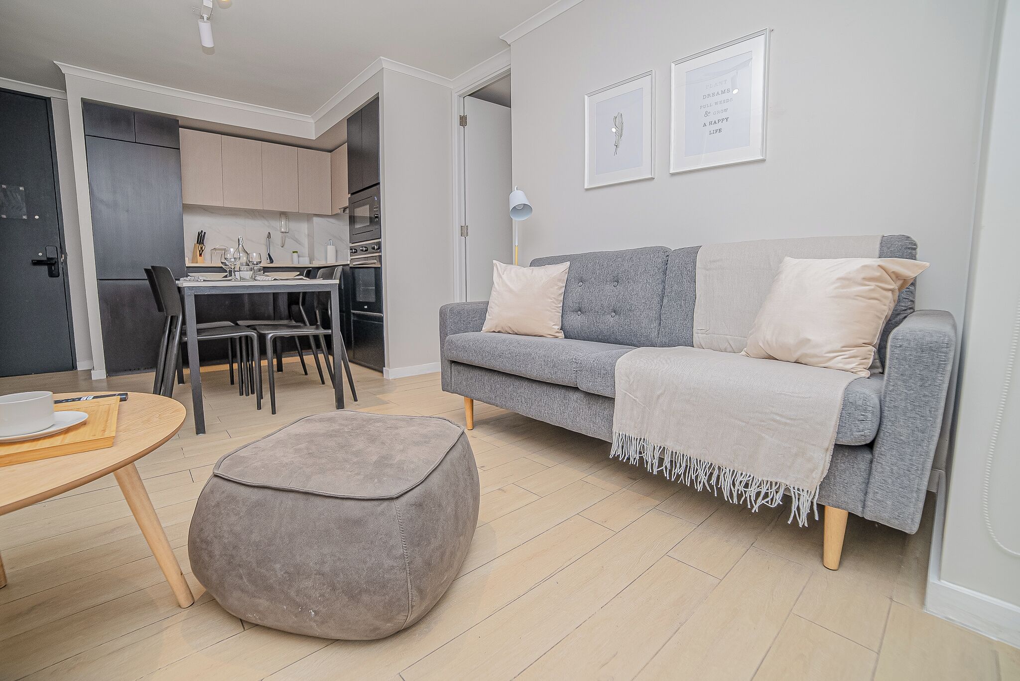 Uma sala de estar moderna com um sofá cinzento, um banquinho e uma área de jantar com mesa e cadeiras.