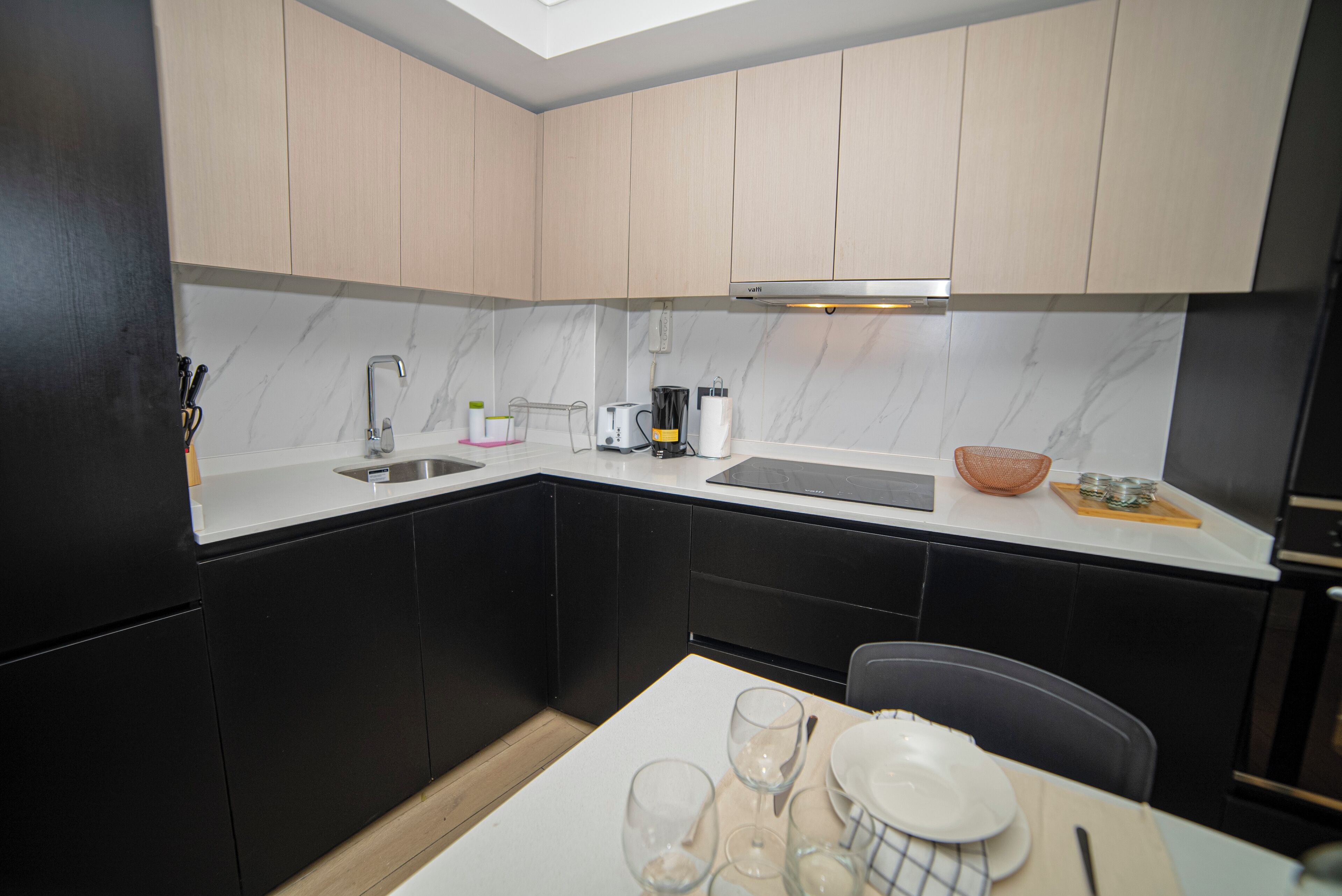 A compact kitchen with black cabinets, a white countertop, and a dining area with a table set for two.