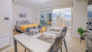 Ein modernes Hotelzimmer mit einem Bett, einer Essecke mit Tisch für zwei Personen und einem großen Fenster mit Blick auf die Stadt.