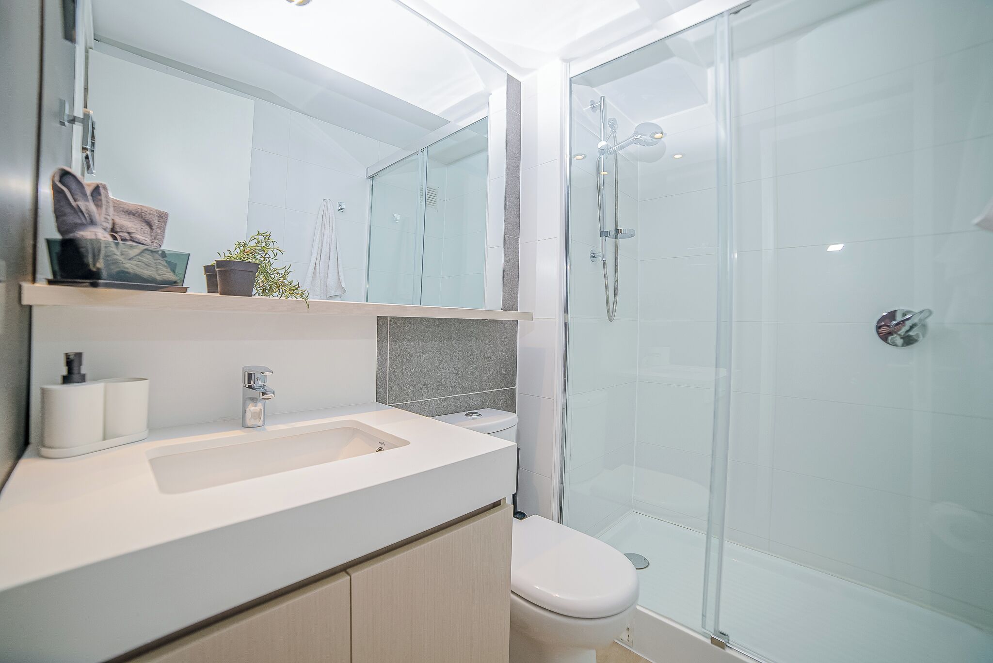 A modern bathroom with a glass shower enclosure, a white sink, and a toilet.