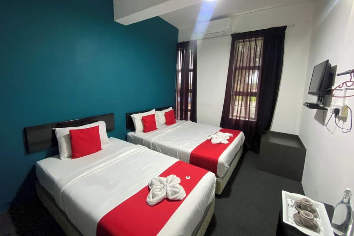 Habitación de hotel con dos camas, paredes verde azulado y un televisor en la pared.