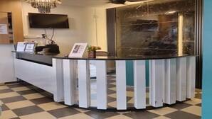 Un espace d’accueil avec un mur en marbre noir, un lustre, un ventilateur de plafond et un sol à carreaux.