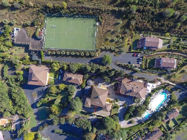 Vista aérea de una zona residencial con un gran campo deportivo, varias casas y una piscina.