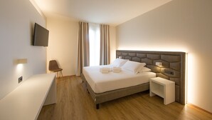 Quarto de hotel moderno com uma cama grande, mesas de cabeceira, televisão de tela plana na parede e piso de madeira.